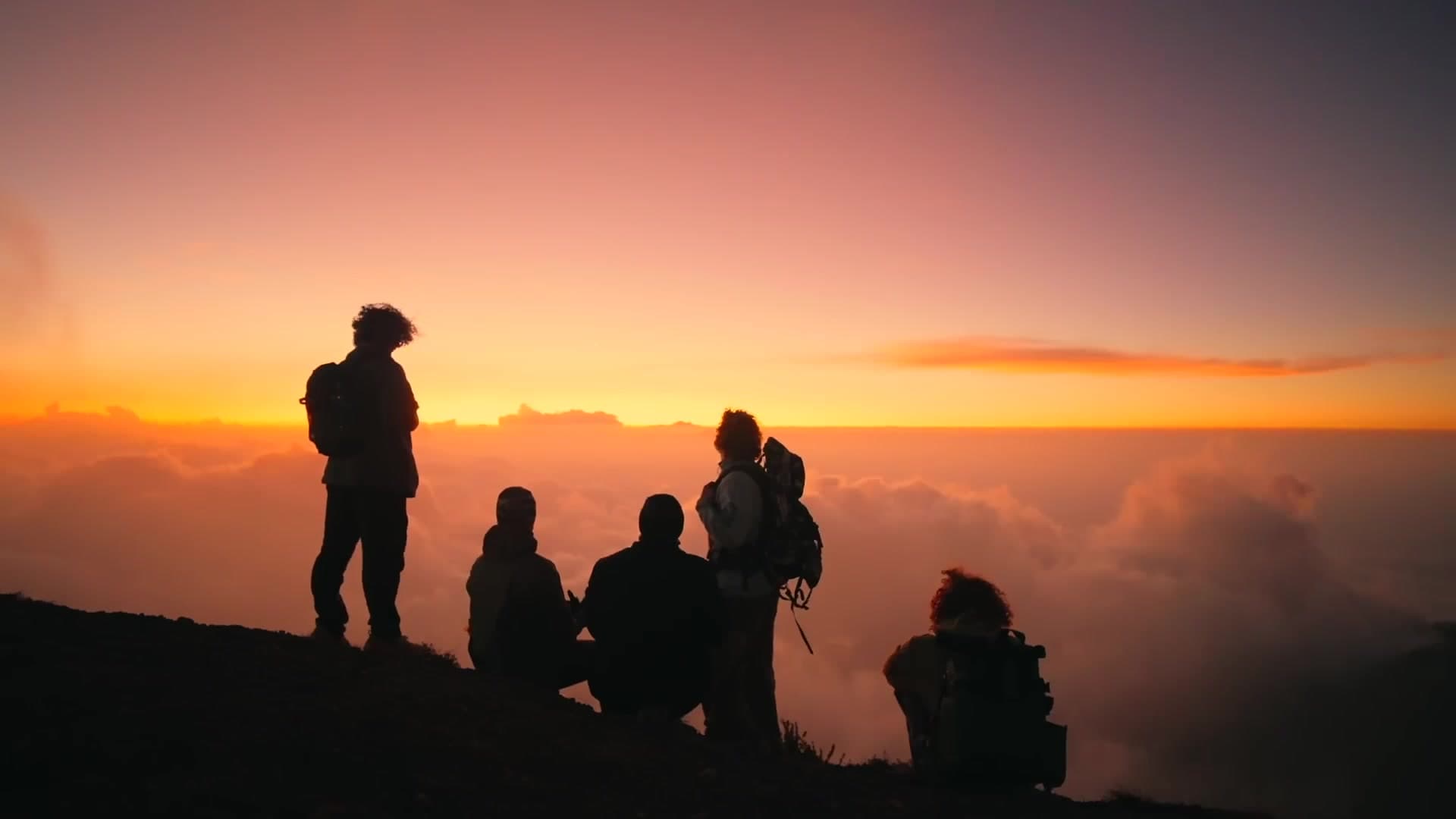 Group of hikers silhouetted above the clouds at sunrise on a volcano summit